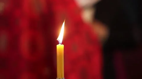 Candle of yellow wax burning flame. It then sees red coat priest officiating Stock Footage 59648581