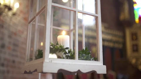 Candlelit lantern beside a window with greenery Видео 336466924