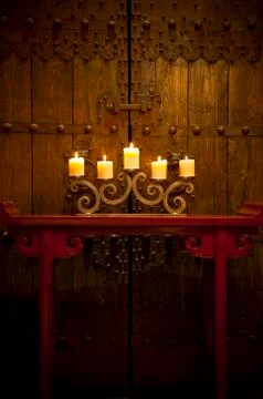 Candles burning on table in front of old rustic door Stock Photos
