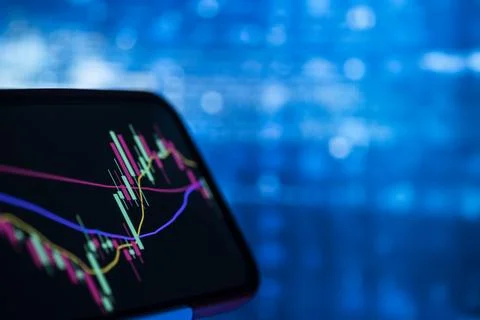 Candlestick stock chart on a smartphone screen against blue bokeh Stock Photos