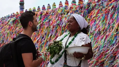 Candomble woman wearing traditional clothes at Bonfim Church blessing a tourist Stock Footage