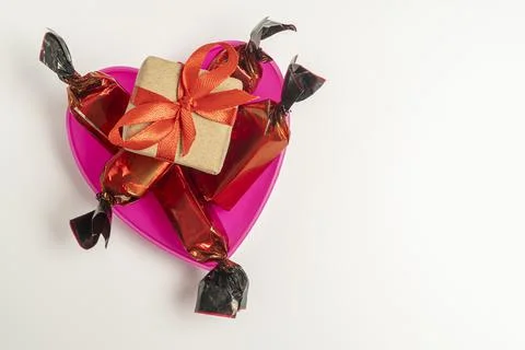Candy and a small gift in a box in the shape of a heart on a light background Stock Photos