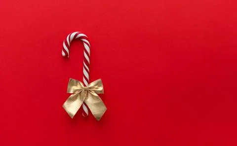 A candy cane with a gold bow on a red tbackground, Christmas Candy. Stock Photos