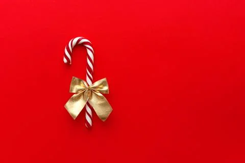 A candy cane with a gold bow on a red tbackground, Christmas Candy. Stock Photos