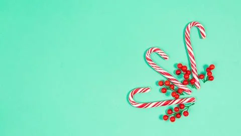 Candy canes are decorated with red berries. Turquoise background. Beautiful h Stock Photos