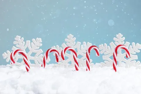 Candy canes in snow against a backdrop of snowflakes and a blue sky Stock Photos