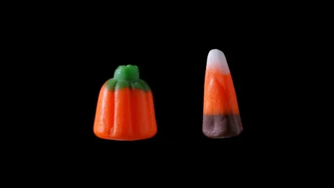 Candy corn and a candy pumpkin are seen floating and rotating with a black Stock Footage 116415619