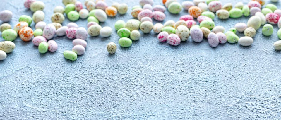 Candy, glazed chocolate Easter eggs sprinkled on a blue background from above. Stock Photos