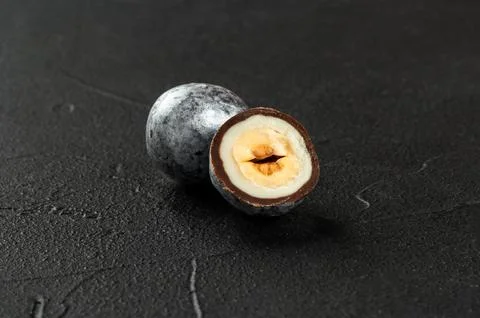Candy hazelnuts in chocolate with a cut half close-up on a dark concrete ba.. Stock Photos