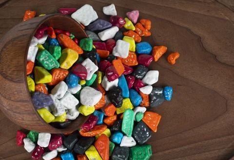 Candy pebbles scattered from small white bowl to coaster on a rustic old burlap Stock Photos