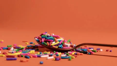 Candy Sprinkles Scattered on Bright Orange Background in 4K Ultra HD Video Stock Footage 314008855