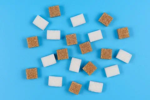 Cane and white sugar cubes on a blue background. Stock Photos