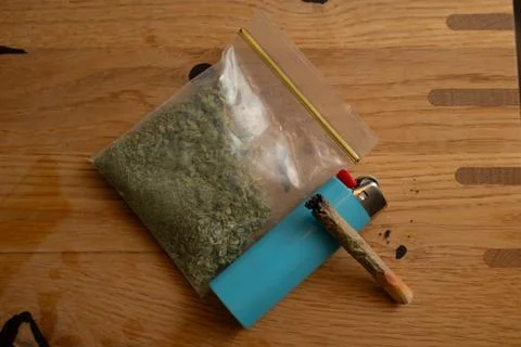 Cannabis marijuana joint and baggie with ground weed next to a blue lighter 库存照片