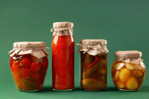 Canned vegetables in jars on a green background. Pickled cucumbers, tomatoe.. Stock Photos
