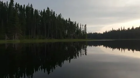 Canoe boat floating on a calm small northern lake as the sun sets behind spruce Stock Footage 320318737