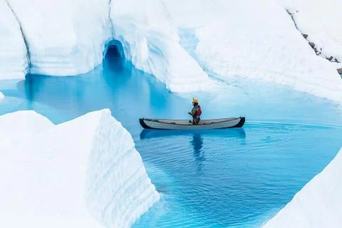 Canoe in front of a small ice cave in the rain. Boating on a glacier lake in Stock Photos