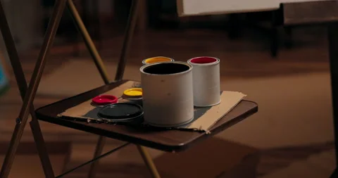 Cans of colored paints stand open on an artist's table near an easel with a Vídeo Stock 161753065