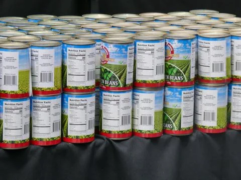 Cans of vegetables lined up on a table with a black table cloth. Stock Photos