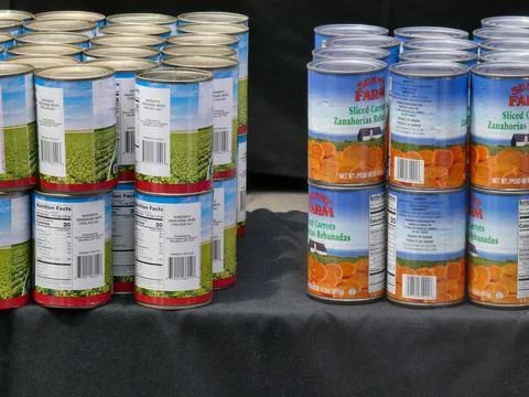 Cans of vegetables lined up on a table with a black table cloth. Stock Photos