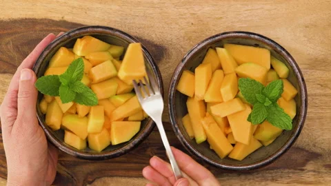 Cantaloupe melon bite-sized cubes served with mint leaves close up in a bowls Video stock 142777156