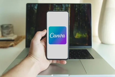 Canva design application logo on smartphone screen in front of laptop Stock Photos