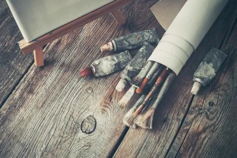 Canvas on easel, paint tubes, bundle of brushes for painting  Stock Photos