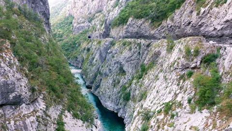 Canyon and road cut in its rocky wall, with a stream at bottom of deep ravine Stock Footage 159828107