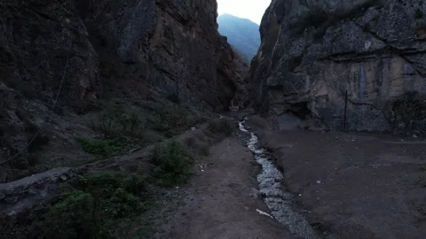 Canyon floor with stream and dirt path between rocky walls under overcast sky Stock Footage 342706171