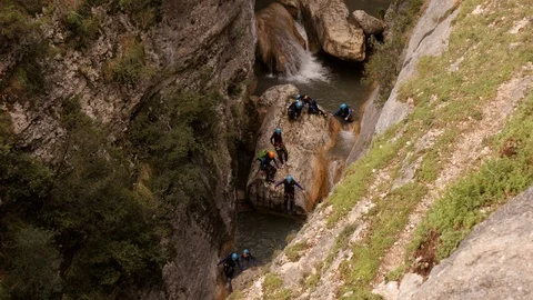 Canyoning group jumping down from a rock into the river -wide shot Stock Footage 98298888