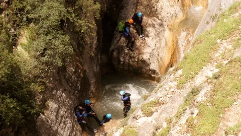 Canyoning group jumping down from a rock into the river -medium shot Stock Footage 98299745