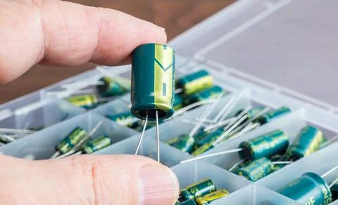 A capacitor held in a hand, with a box of capacitors in the background. Foto stock