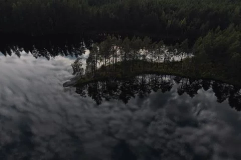 Cape with pine trees. The clouds are reflected in the lake. Evening time Foto stock