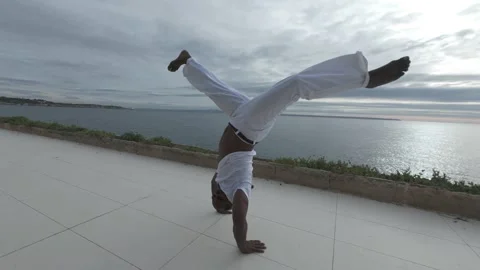 Capoeira artist practicing dynamic movements by the seaside Stock Footage 295801681