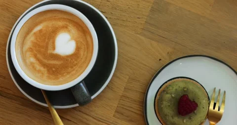 Cappuccino with heart pattern and tasty small cake served on wooden table Stock Footage 312620656