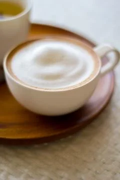 Cappuccino in a white cup on a white plate on wood table Stock Photos