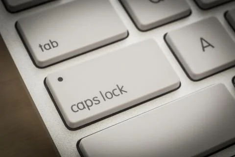 Caps lock button on white keyboard, dark filter. Stock Photos