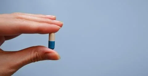 Capsule between the fingers on a blue background, medication, medical worke.. Stock Photos