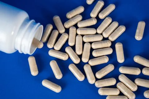 Capsules pouring from an open plastic bottle onto a blue surface. Concept of Stock Photos