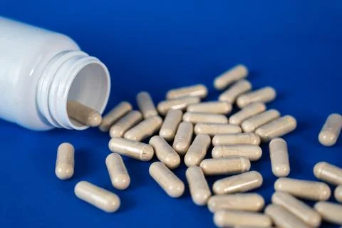Capsules spilling from open bottle on blue background Stock Photos