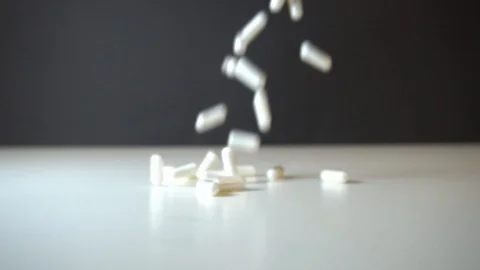 Capsules with supplements or medicine falling on a white table in front of a  Stock Footage 122592089