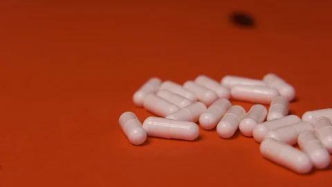 Capsules, white black tablets lie, roll on a red table, background, medicine Stock Footage 125351728