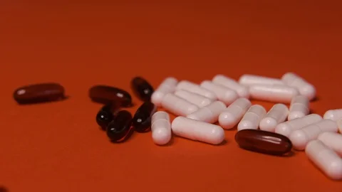 Capsules, white black tablets lie, roll on a red table, background, medicine Stock Footage 125351735