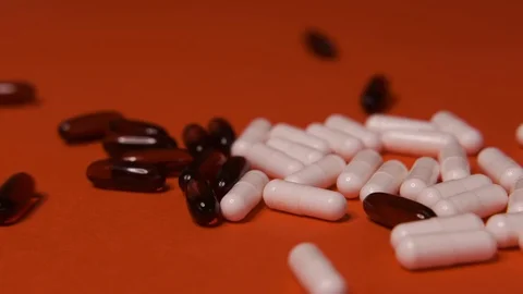 Capsules, white black tablets lie, roll on a red table, background, medicine Stock Footage 125351763