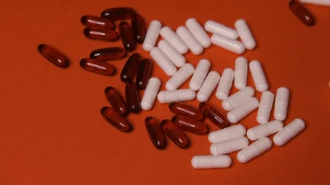 Capsules, white black tablets lie, roll on a red table, background, medicine Stock Footage 125351780