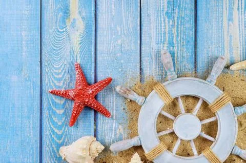 Captain steering wheel on shells and starfish on rustic border Stock Photos