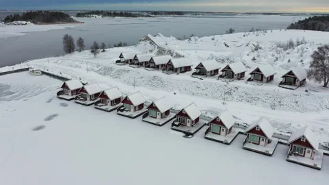 Captivating camera pan over snow-covered cabins nestled by a frozen lake, aerial Stock Footage 292965806