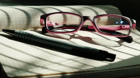 A captivating close-up of eyeglasses and a pen resting on an open notebook .. Stock Footage 334591602