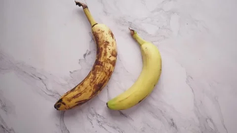 A captivating close up shot of two bananas, one yellow and ripe, other brow.. Vídeos de archivo 332626352