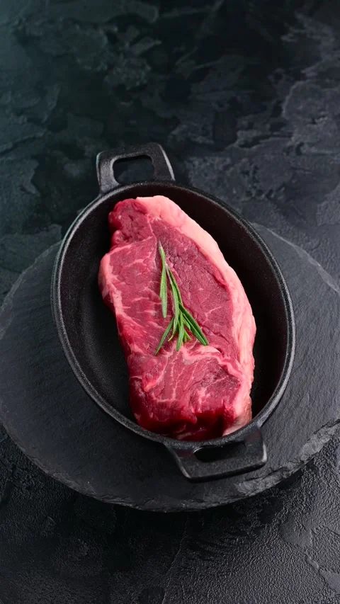Captivating preparation of fresh steak with rosemary on black slate Stock Footage 305233379