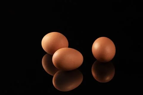 Captivating reflection of brown chicken eggs on black mirrored surface Stock Photos